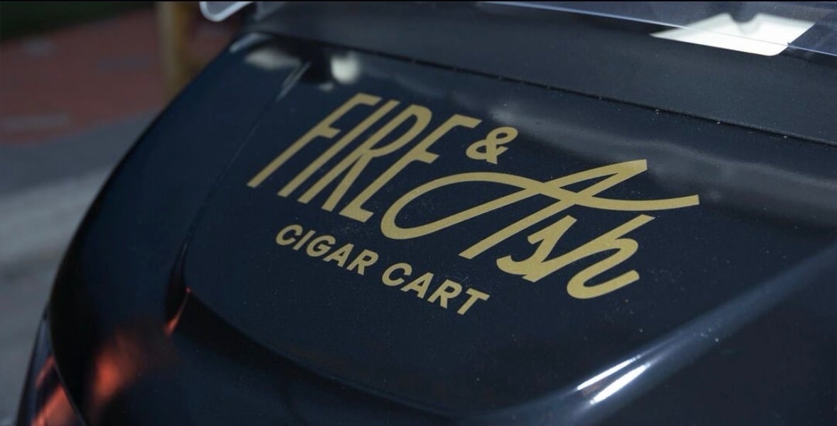 Gold lettering reading Fire and The Cigar Cart on a black curved surface